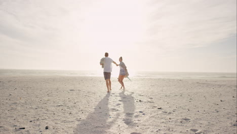 Young-couple-holding-hands-walking-towards-sunset-on-empty-beach