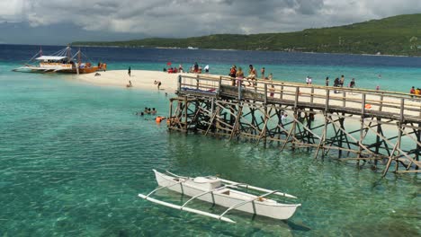 people enjoy a sunny day by the clear waters of sumilon island with boats and a wooden pier in view