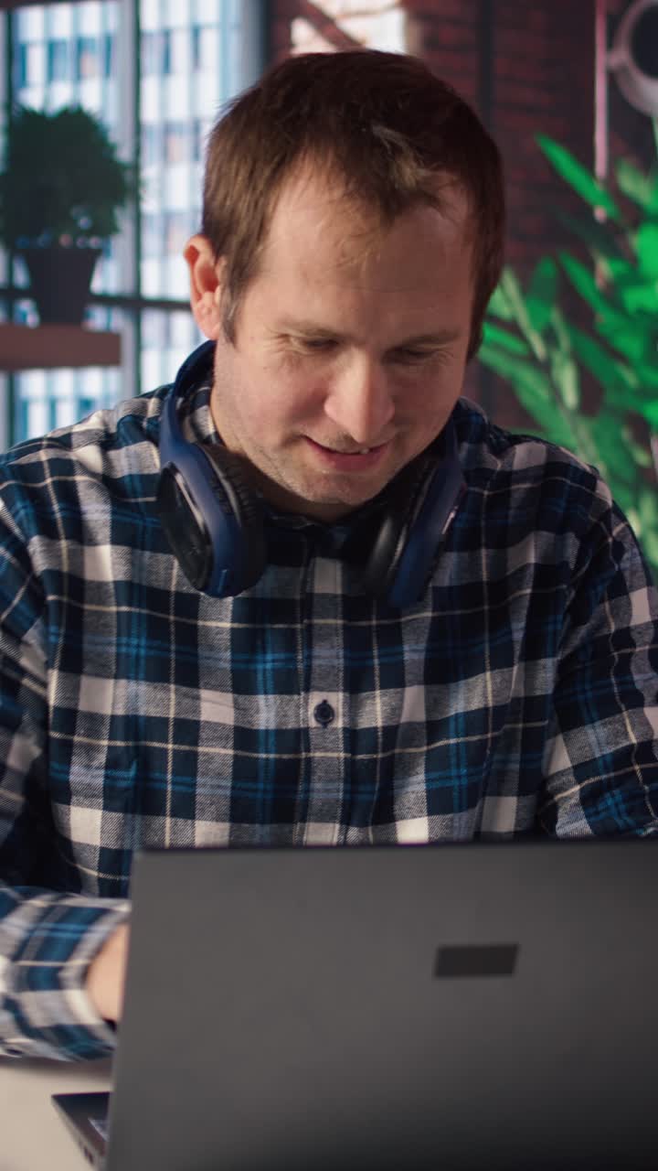 Vertical video Man enjoying leisure time at home, texting friends on laptop