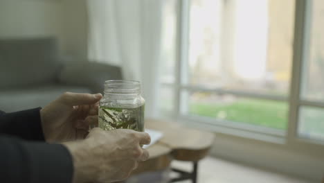 man holding herbal tea glass in apartment with a garden