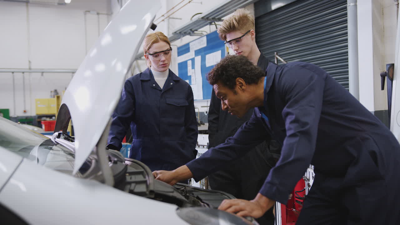 tutor masculino con estudiantes mirando el motor del coche en el curso de aprendizaje de mecánico de automóviles en la universidad