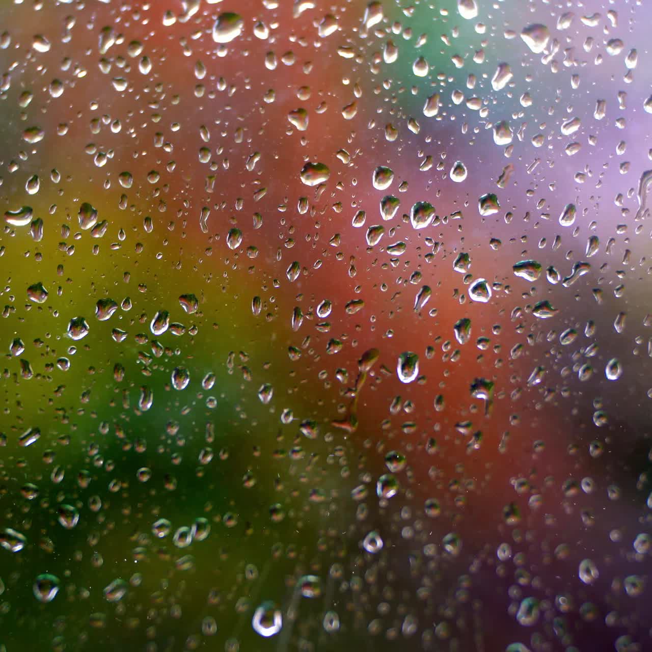 Glass with raindrops. Water drops on window on blurred colorful background. Rain falling outside. Droplets background. Close-up.