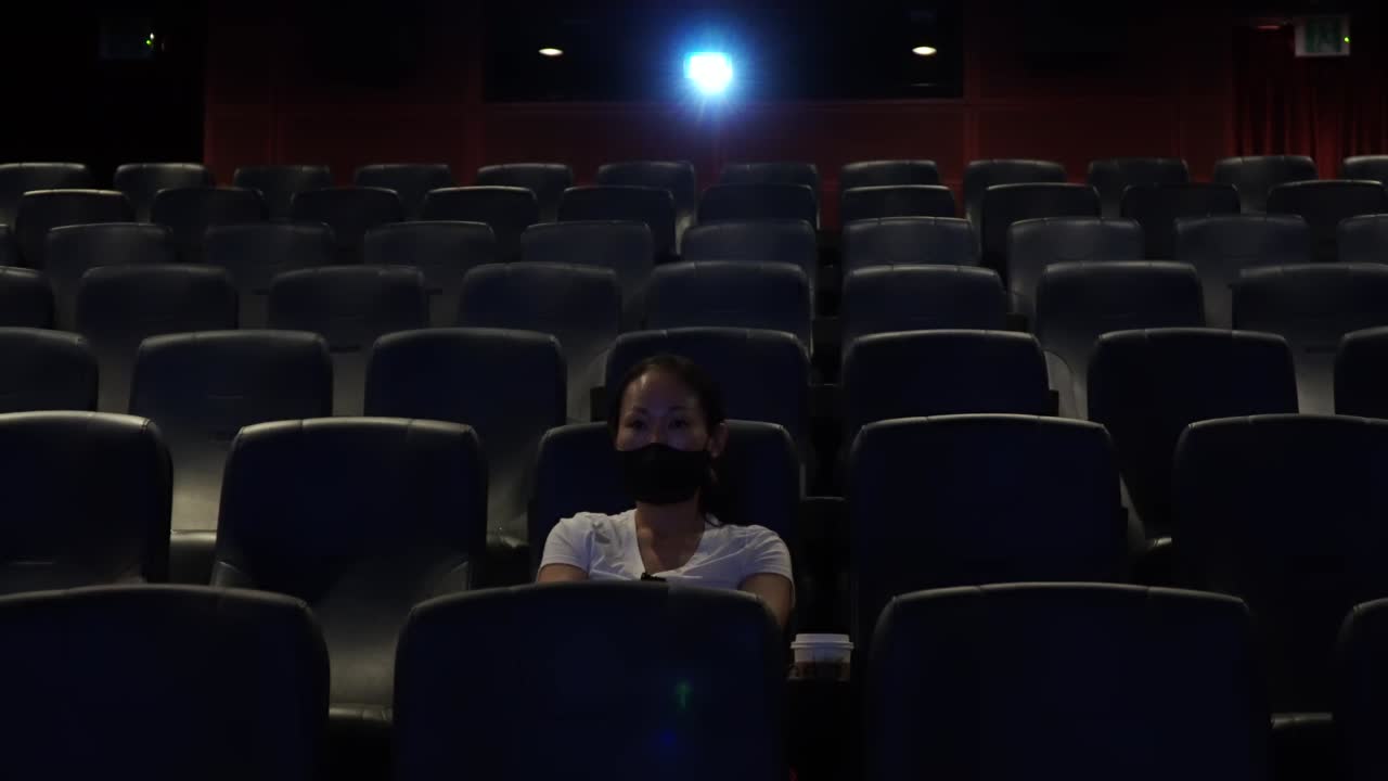 Front View Of A Korean Woman Sitting Alone In The Dark Cinema And Watching Movie After A Long Day with Nobody Around during Covid-19 Coronavirus Pandemic in South Korea wide