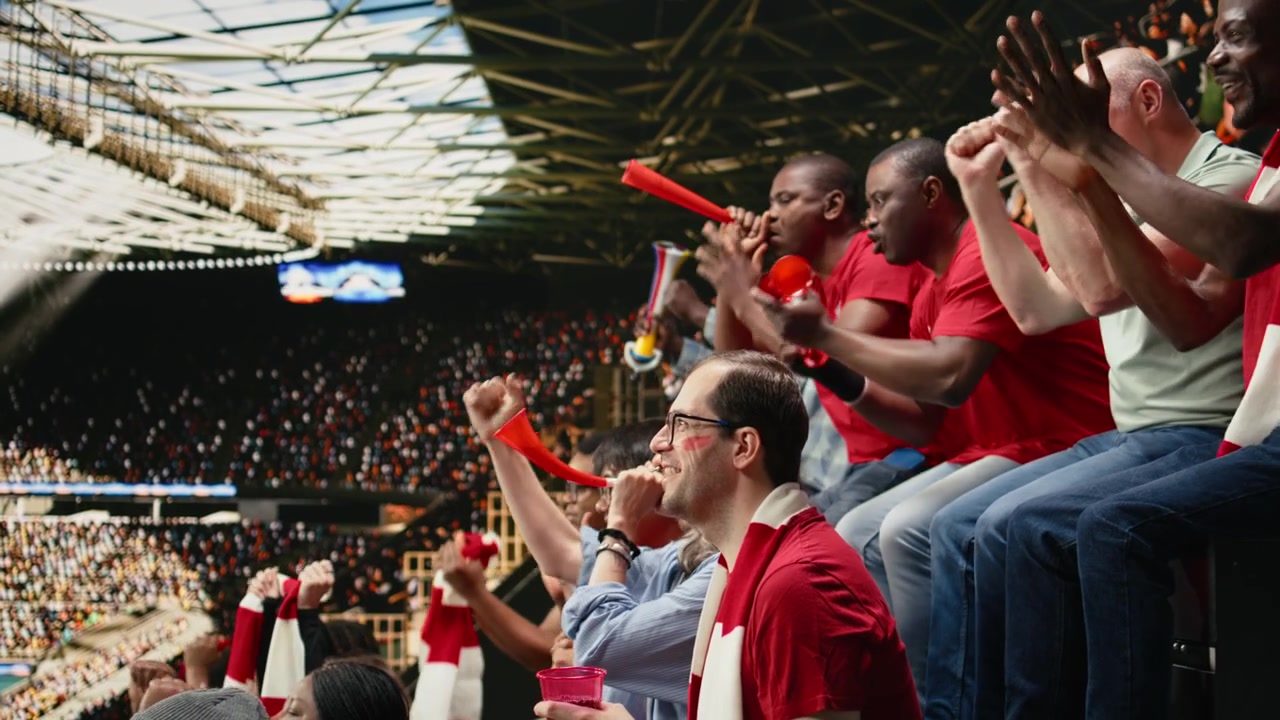Diverse red team soccer fans watching live football match from stadium stands