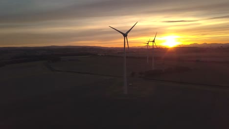 Aerial-parallax-shot-of-a-line-of-wind-turbines-spinning-on-a-field-at-sunset