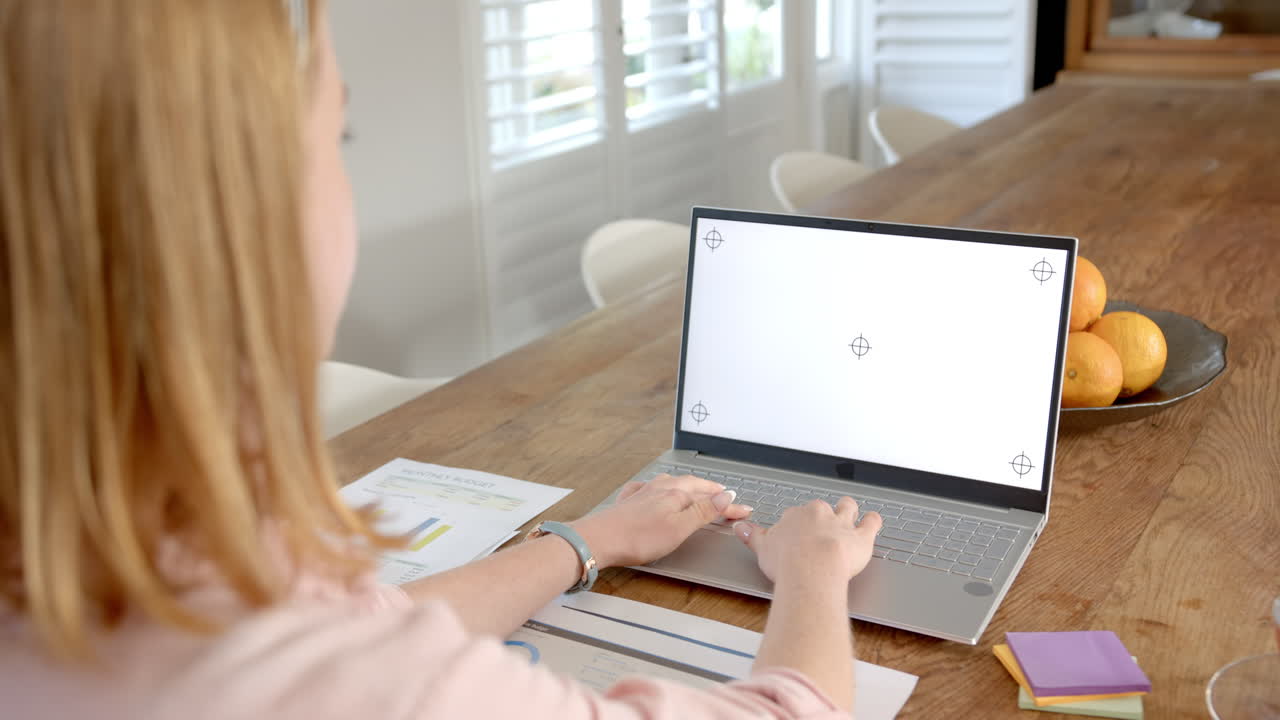 Working from home, woman using laptop and analyzing documents on wooden table, copy space