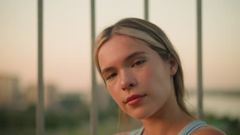 white lady posing in front of camera with a warm smile, with blurred iron railing and city view in background, with soft natural lighting highlighting her facial features