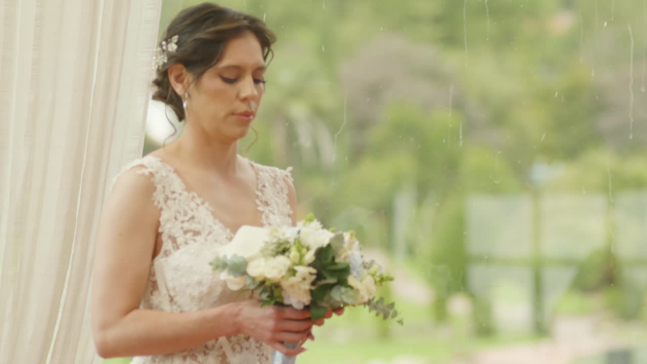 Medium shot of a bride walking with a bouquet of flowers, wearing a lace dress as she heads to the ceremony.