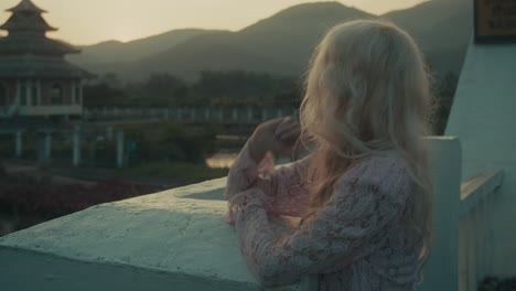 blonde woman in pink lace dress by asian temple at sunset
