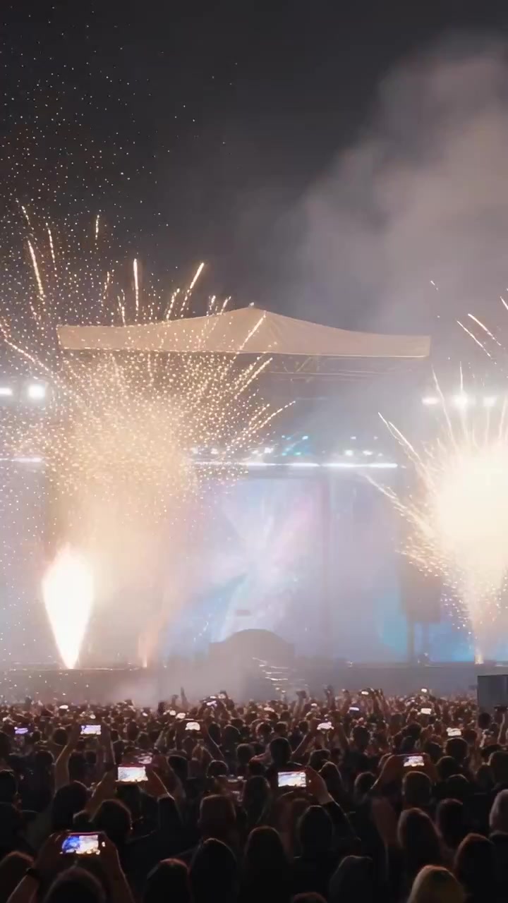 Video verticale: Fuochi d'artificio che sparano scintille dorate attraverso il palco del concerto, telefoni che filmano il finale.