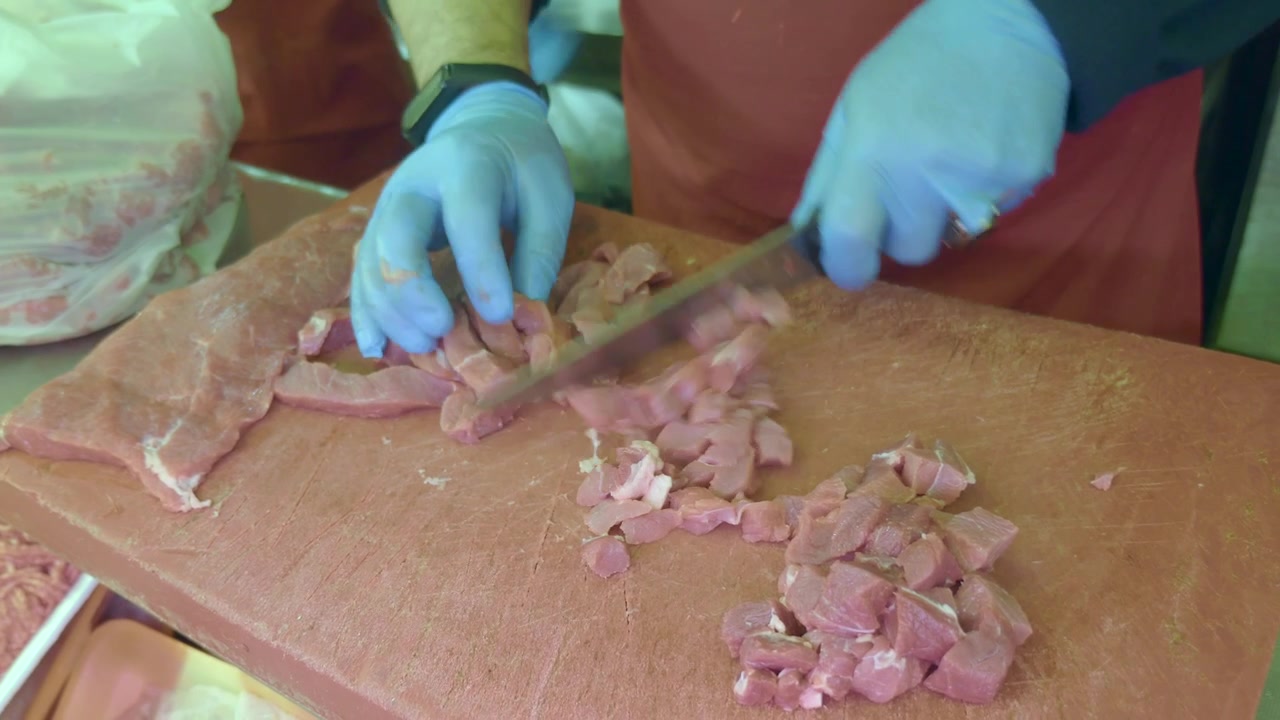 Carnicero con guantes azules cortando carne roja cruda en una tabla de cortar