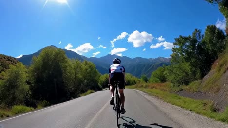 A man is riding a bicycle down a road with mountains in the background