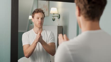 Portrait-of-a-man-in-the-mirror-applying-cream-on-his-hands-and-spreading-massage-movements