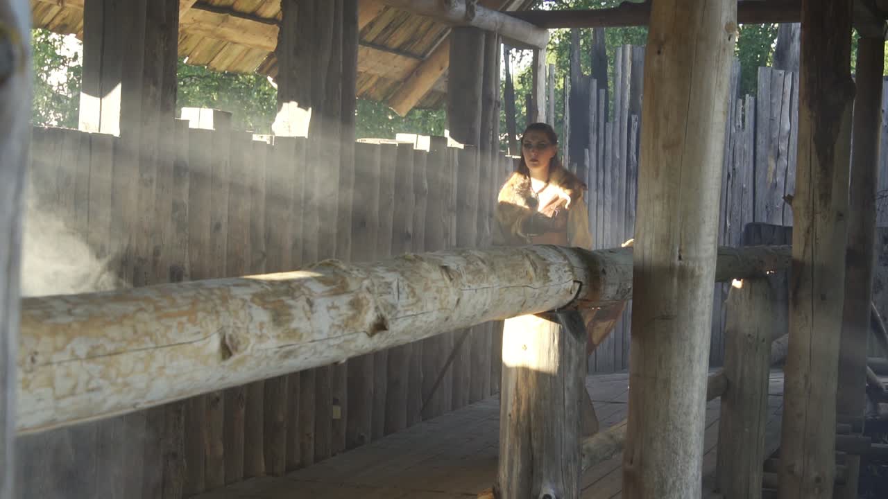 바이킹 여성 전사는 나무 테두리, 연기 및 태양 광선을 통해 난간을 걷습니다.