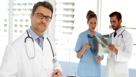 Doctor-looking-at-clipboard-then-smiling-at-camera