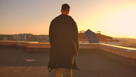 Hacker-using-laptop-on-rooftop-with-city-view-and-forex-chart.-Hacking-and-stats-concept.-A-man-at-sunset-in-slow-motion-writing-software-code-on-a-laptop