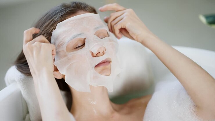 Young domestic woman posing apply tissue face mask for skin care while lying in the bath