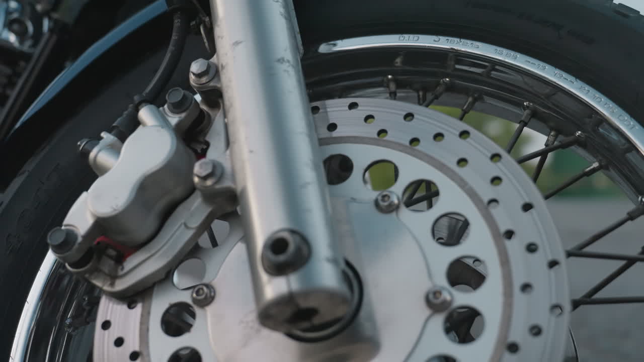 Close up parked motorbike with shiny chrome headlight and orange indicator captured beside roadside while truck passes in blur background of greenery under evening sky