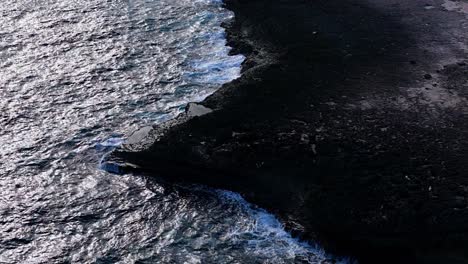 slow orbit around strong ocean waves crashing on basalt rock point with eroded grooves in the earth