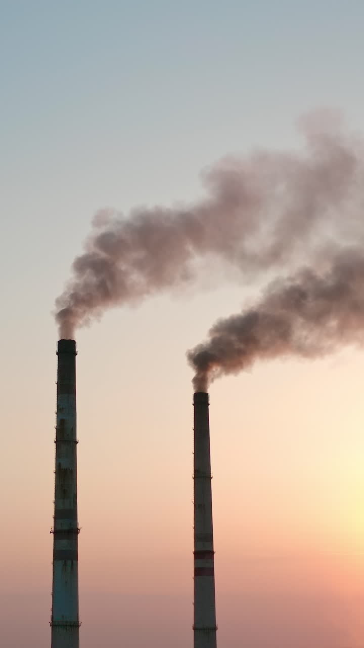 Smoke pipes on clear evening sky background. Factory chimneys release dark emissions into the atmosphere. Chemical smoke pollute the air. Ecology in danger. Vertical video
