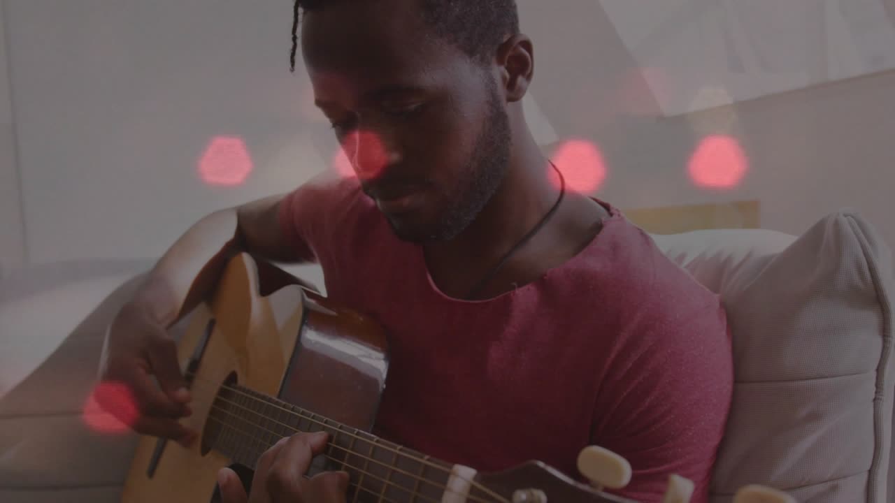Un uomo che posiziona le dita, pizzica e strimpella, esercitandosi con la musica mentre un bokeh esagonale rosso fluttua sulle mani