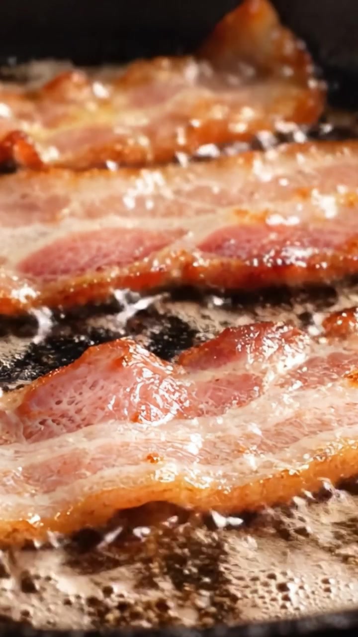 Sprøde baconstrimler steger til perfektion på en stegepande, der fanger den gyldenbrune tekstur og det saftige fedt i lækre detaljer
