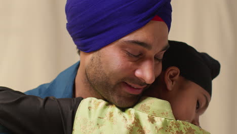 close up studio shot of sikh father embracing son both wearing turbans against plain background 5