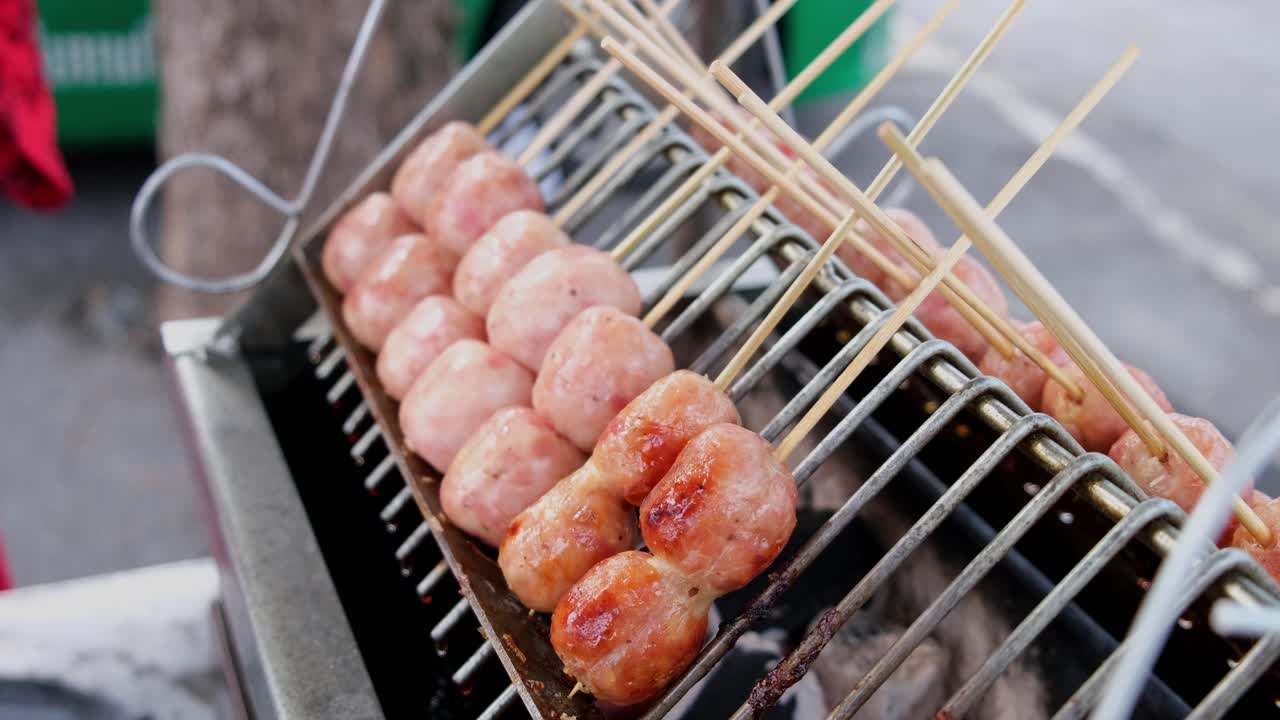 salchichas cortas con carne y arroz torcidas juntas a la parrilla en carbón como se ve una mano ajustándolas, comida callejera a lo largo de la carretera sukhumvit en bangkok, tailandia