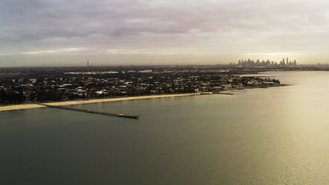 Hermoso-Paralaje-Aéreo-Del-Paisaje-Urbano-Girando-Alrededor-De-Un-Largo-Muelle-De-Madera-Durante-La-Luz-Dorada-De-La-Mañana