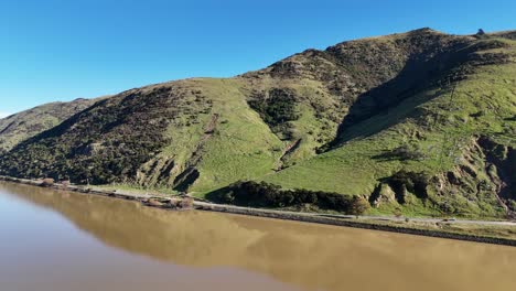 drone footage captures scenic hills and tranquil lake in akaroa, new zealand, under clear blue skies