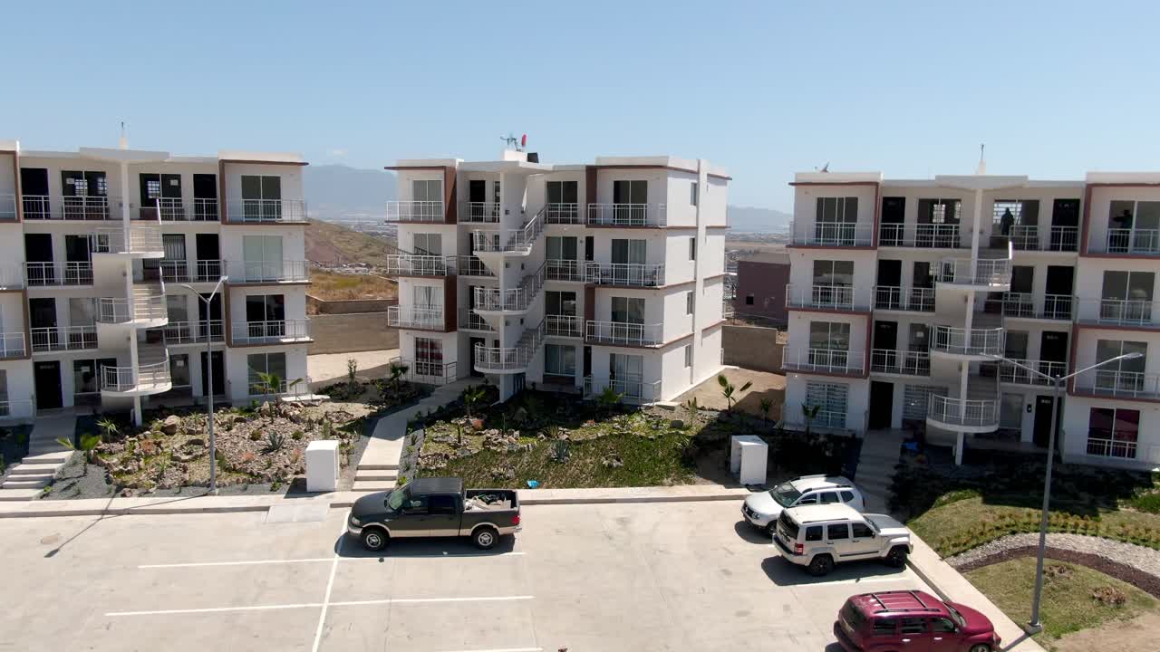 Drone si alza sopra parcheggi ed edifici residenziali rivelando le montagne a Ensenada.