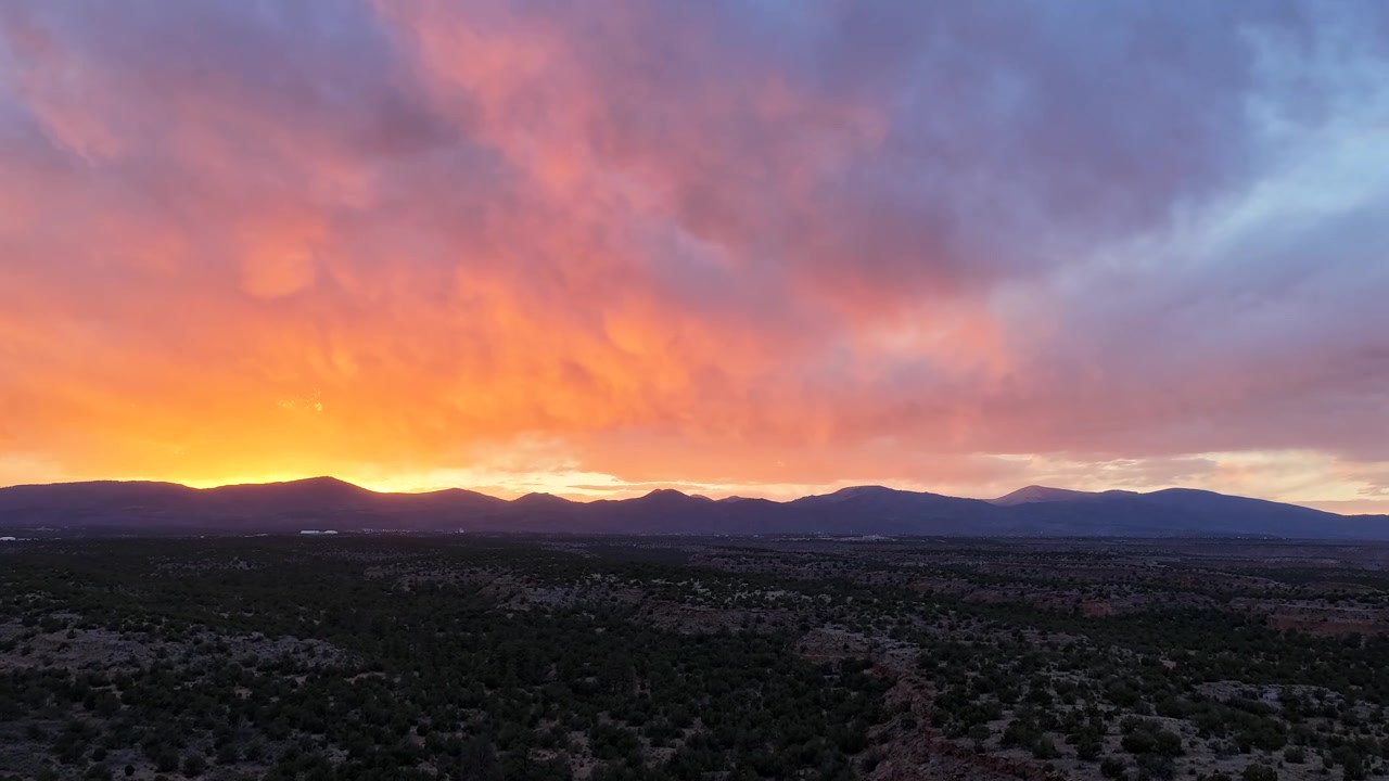 4K drone timelapse captures vibrant orange sunset clouds and intense shifting light over the southwest desert. Cinematic skyscape transition featuring atmospheric glow and wilderness scenery.
