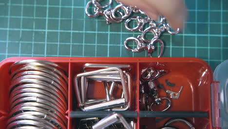 Skilled tailor takes silver clasps from red container close