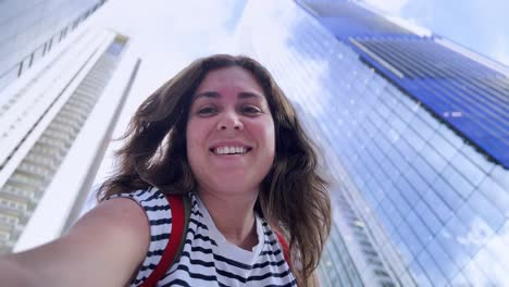 smiling woman taking a selfie in front of skyscrapers