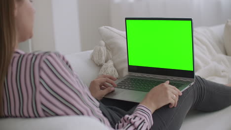 una mujer joven y relajada está usando una computadora portátil con pantalla verde para la tecnología chroma key para chatear en internet llamando por video chat