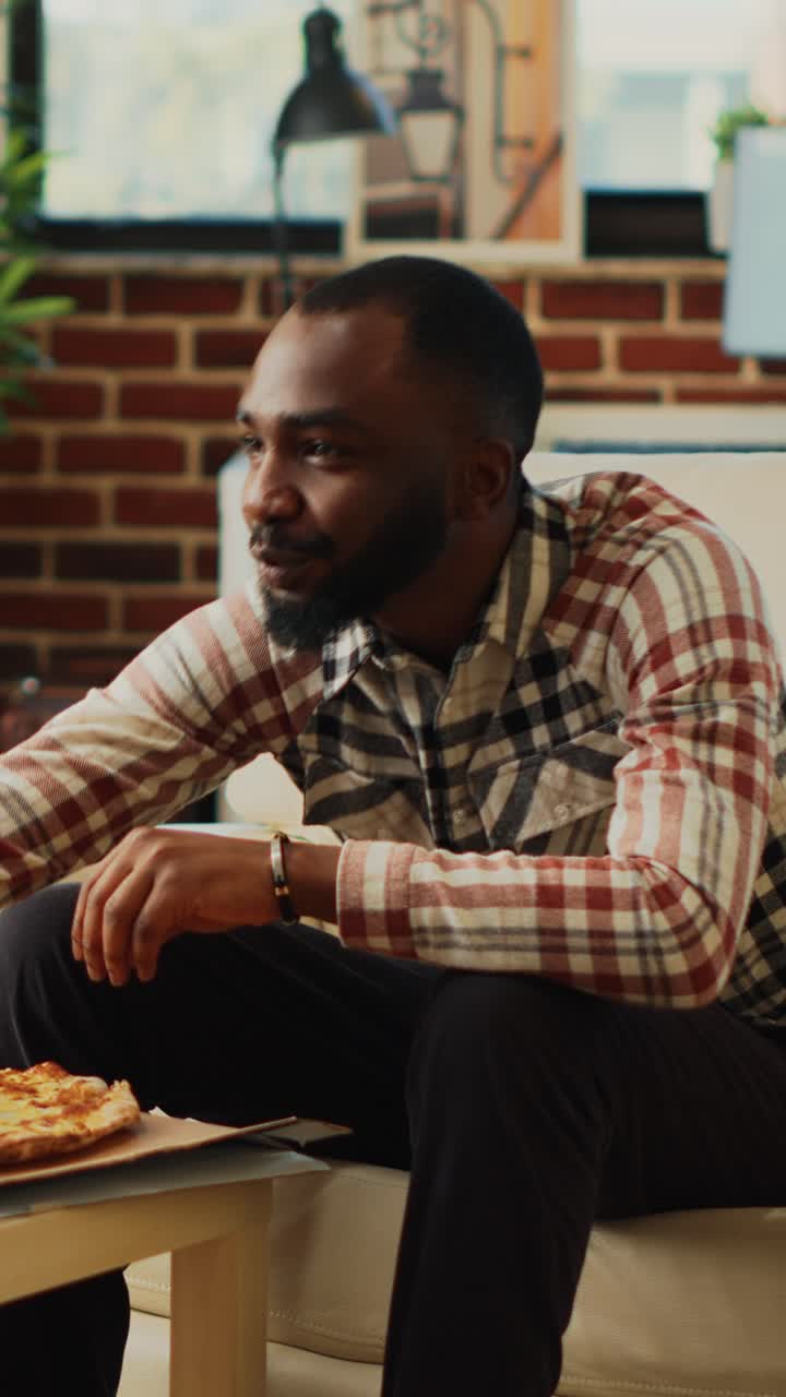 Vertical video: African american guy eating slices of pizza from takeout