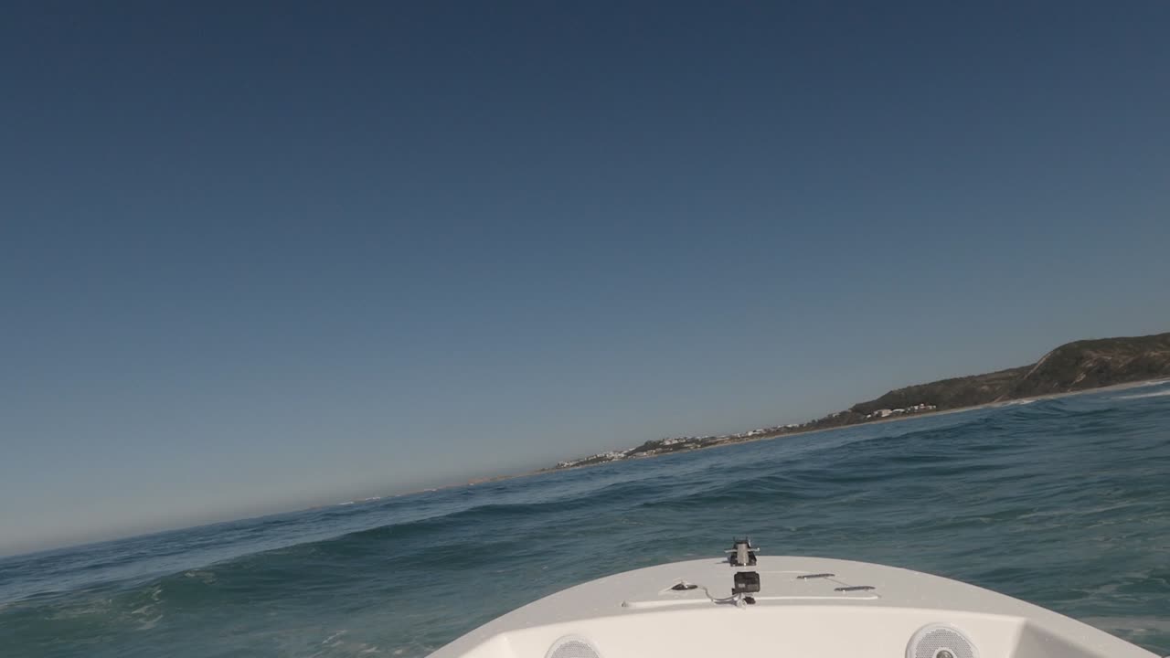 FPV: Powerful motorboat jumps ocean wave crests near shore, sunny day