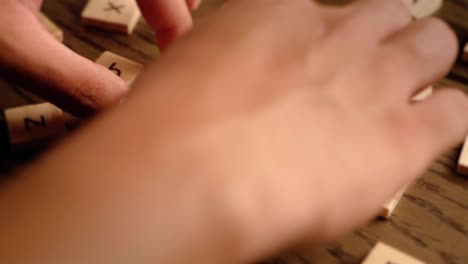 A hand carefully places wooden tiles to spell the word beauty on a wooden surface in warm lighting.