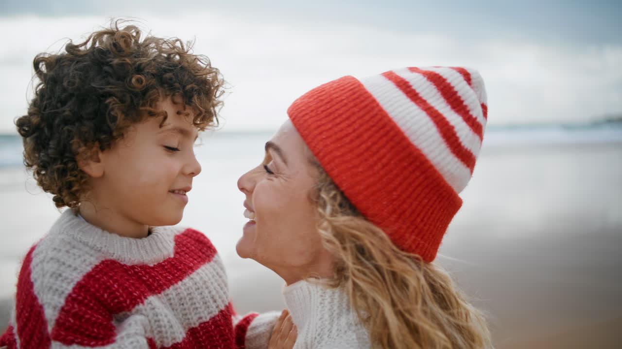 Cute boy kissing mother nose on ocean beach closeup. Motherhood bonding moment.
