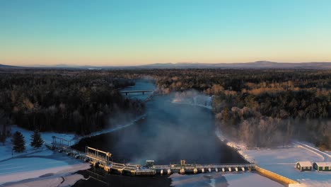 imágenes aéreas que vuelan sobre la presa en un lago congelado dejando que el agua humeante fluya hasta el río de salida durante un amanecer de invierno