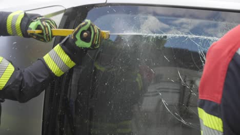 firefighter vigorously cuts through crashed car glass to save trapped person