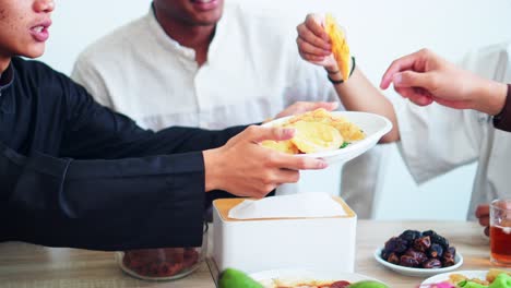 close up view of muslim man passing his friends food during iftar on ramadan at dining table