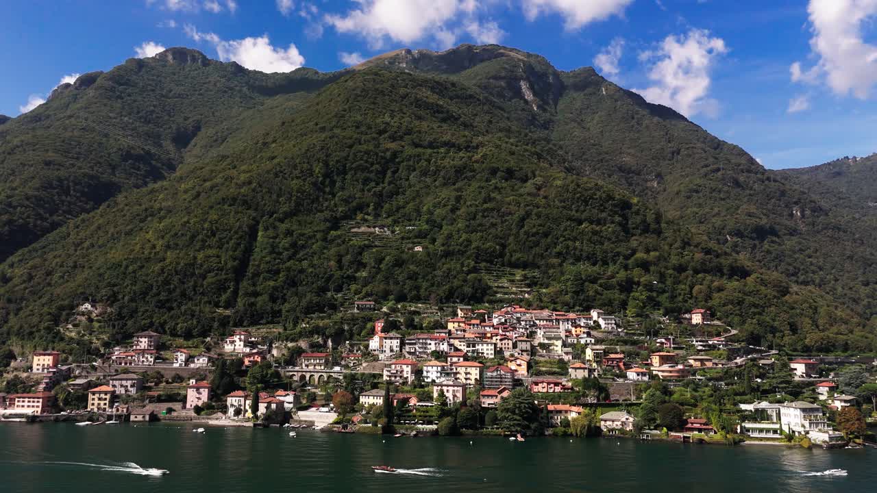 Fly sideways, view of green mountain, blue sky, houses and Lake Como