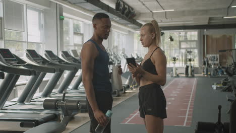 una mujer caucásica y un atlético afroamericano hablando en el gimnasio.