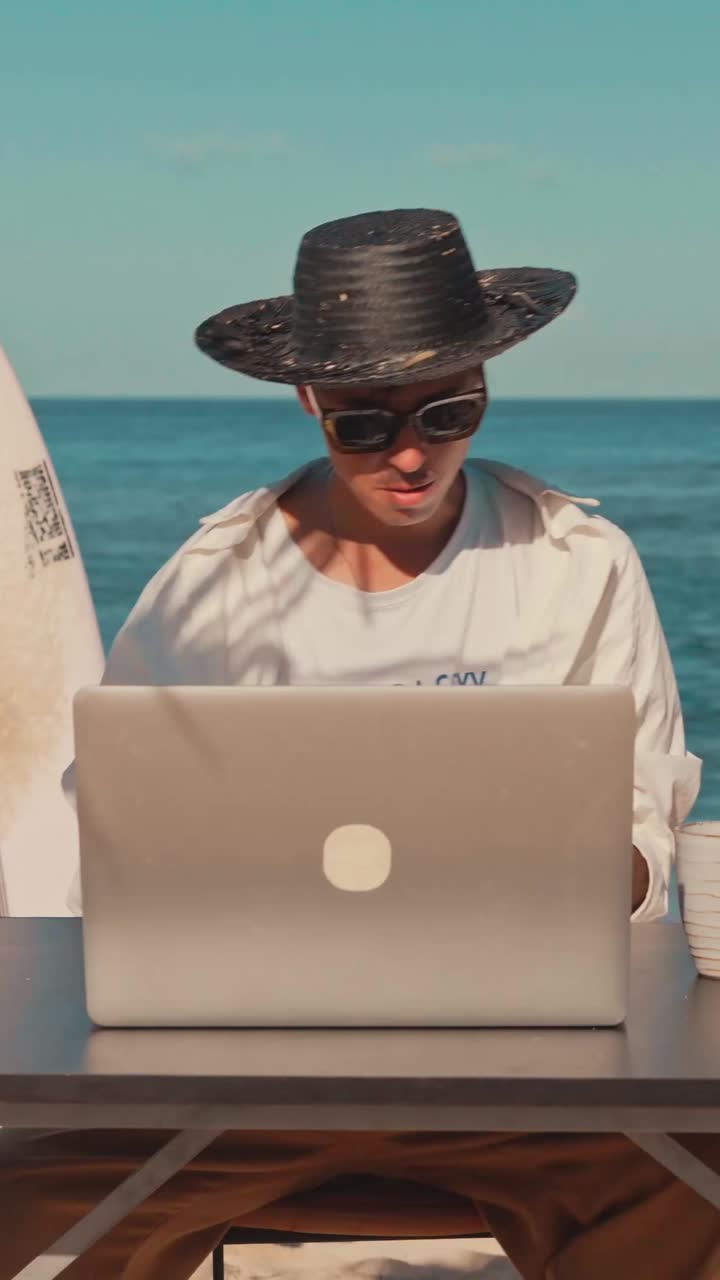 Young caucasian man working in open air beach office sits at desk with laptop