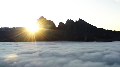 aerial tracking shot revealing the morning sun behind mountains in a foggy valley