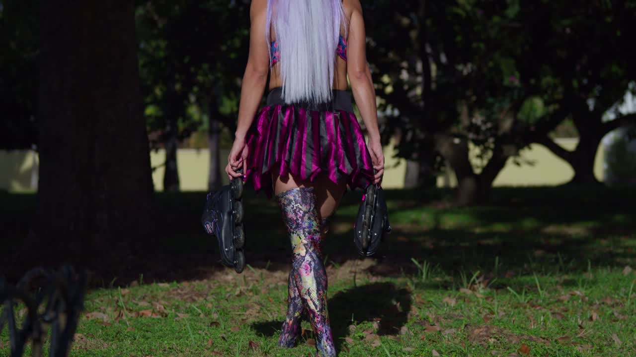 una mujer caminando en el parque mientras sostiene sus patines en una minifalda y polainas