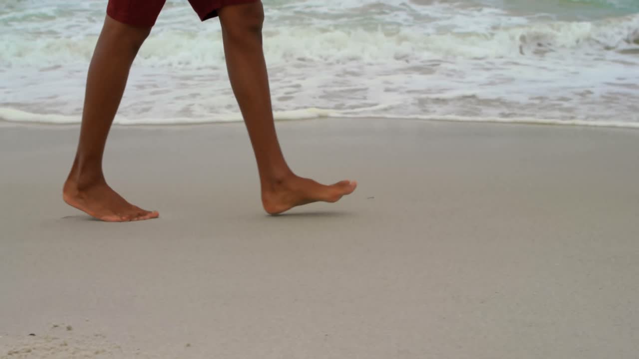 Parte inferiore del corpo di un uomo che cammina a piedi nudi sulla spiaggia in una giornata di sole 4k