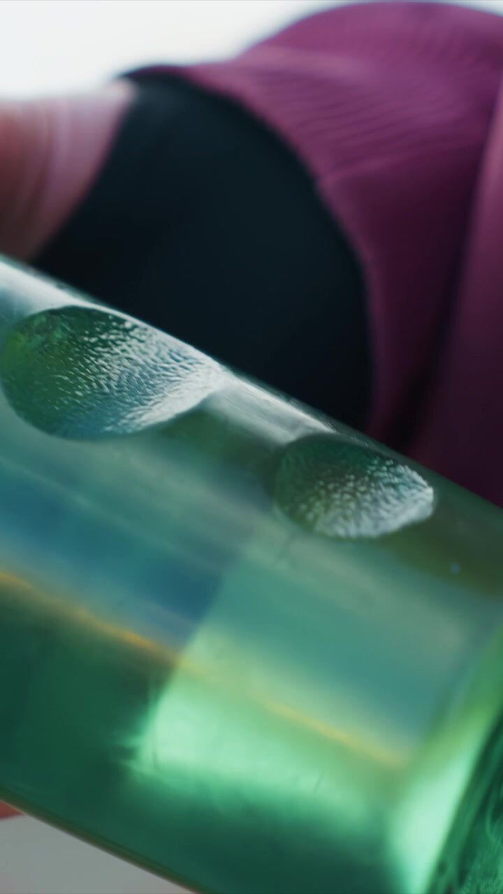 Close up view shows hands holding and rotating transparent or semi transparent plastic green cylindrical shape with distinct circular features. focus remains on object texture color