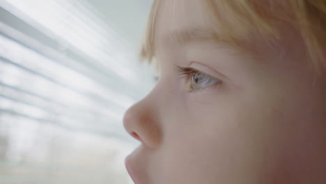 cerca de una niña de ojos azules mirando por la ventana y jugando con las persianas